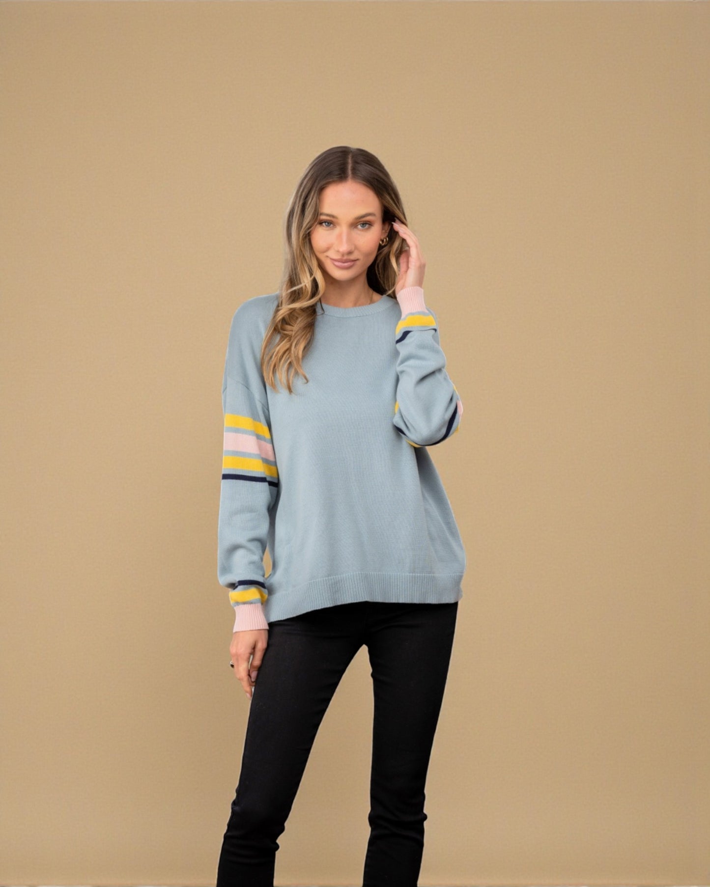 Woman wearing a light blue sweater with yellow stripes on a beige background