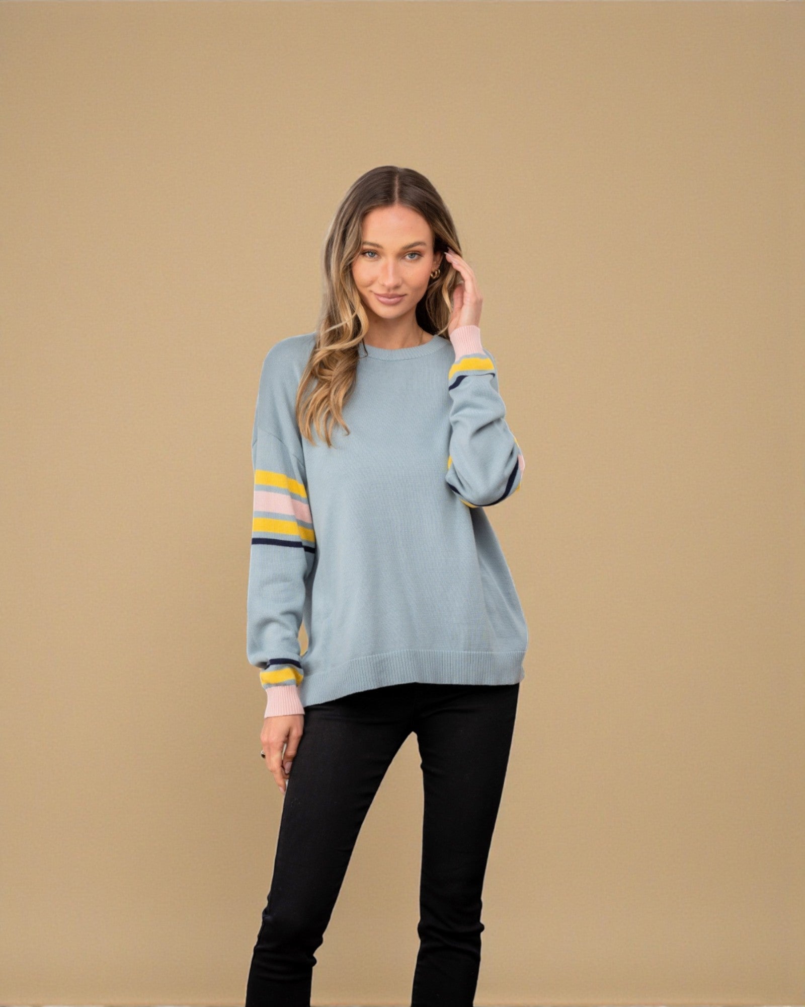 Woman wearing a light blue sweater with yellow stripes on a beige background