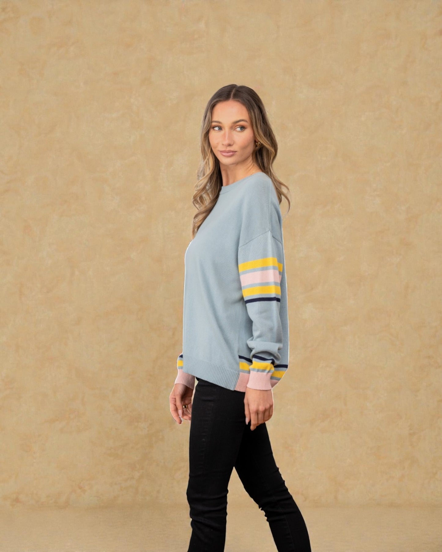 Woman wearing a light blue sweater with colorful stripes on a beige background
