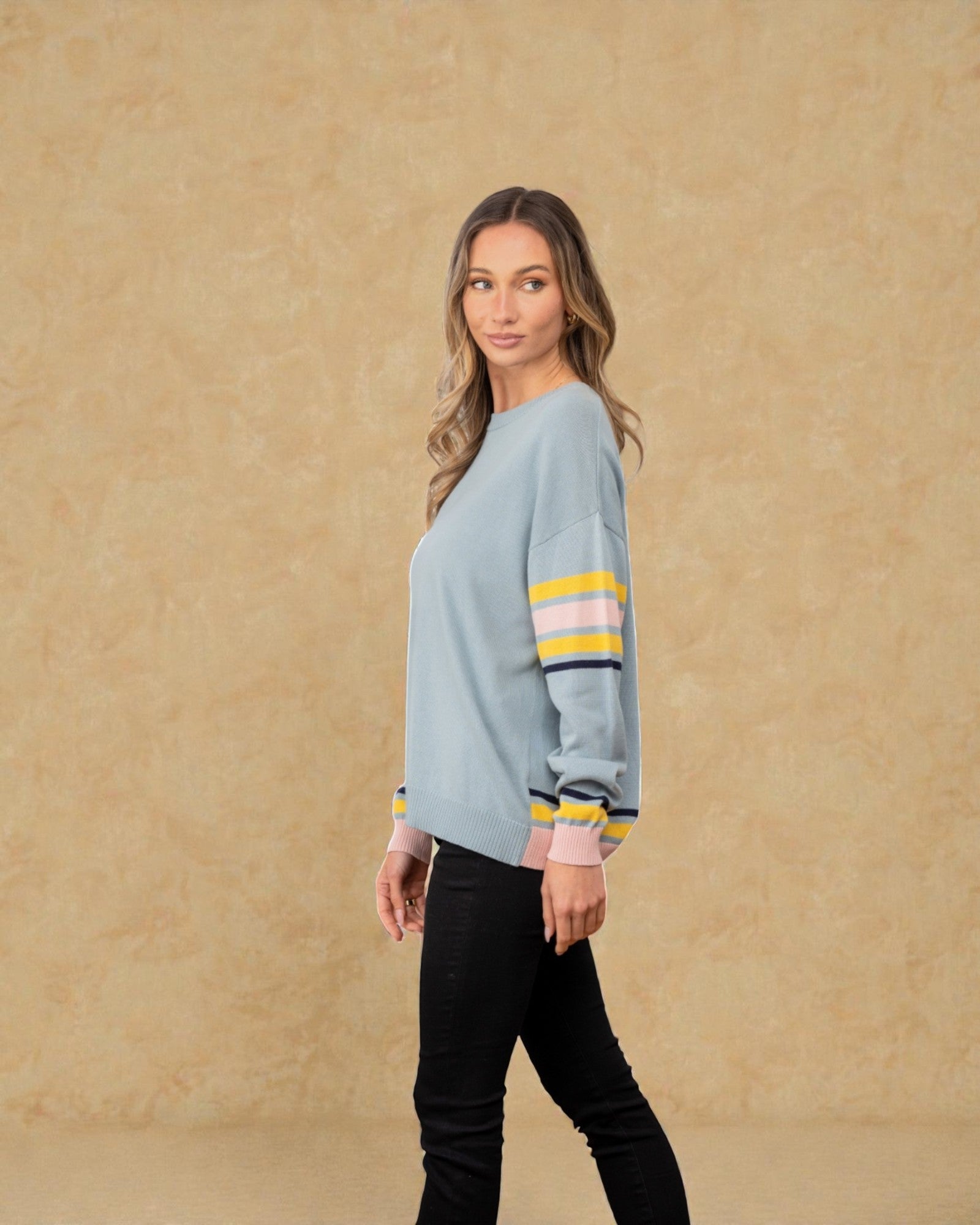 Woman wearing a light blue sweater with colorful stripes on a beige background