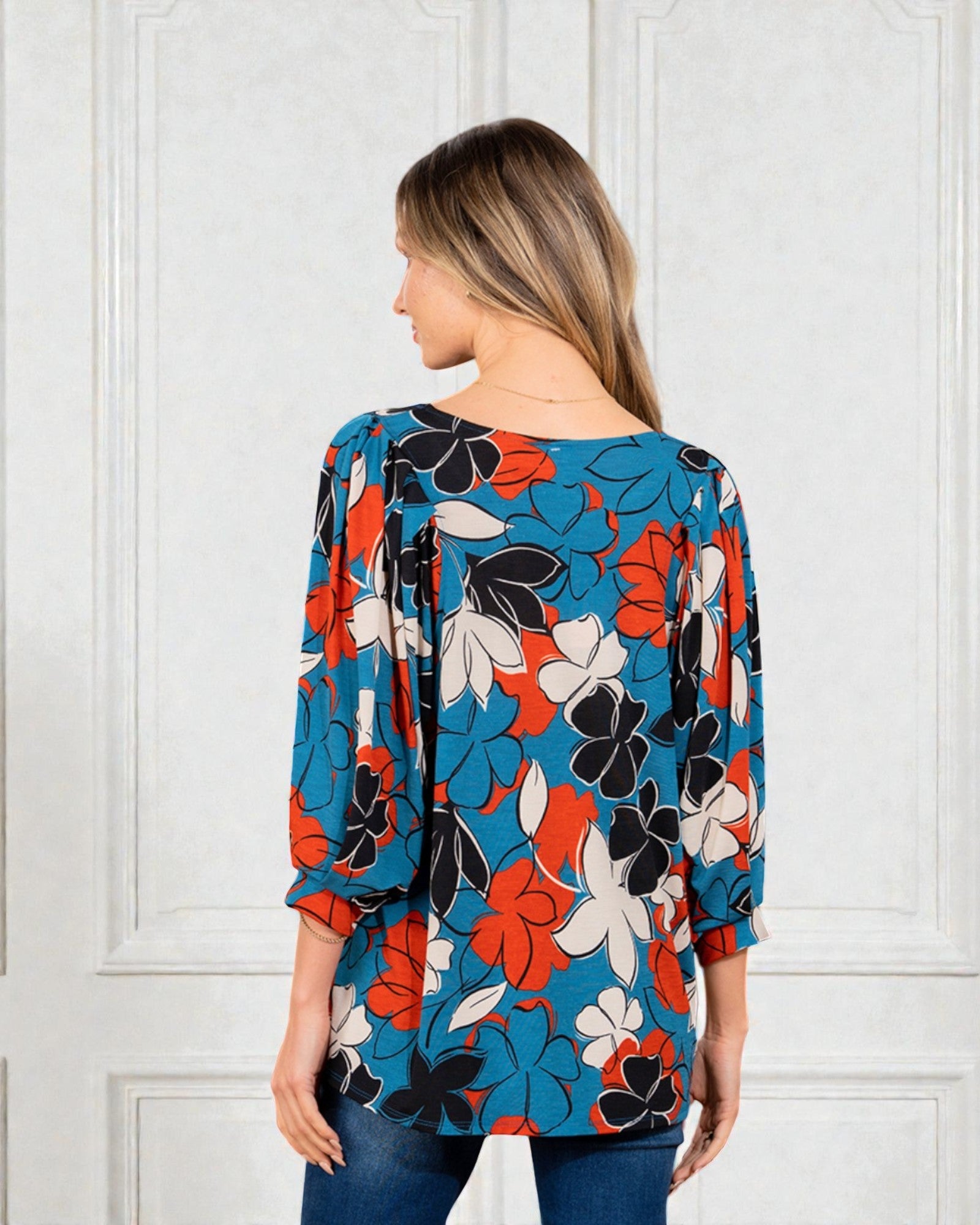 Woman wearing a colorful floral blouse against a white paneled wall
