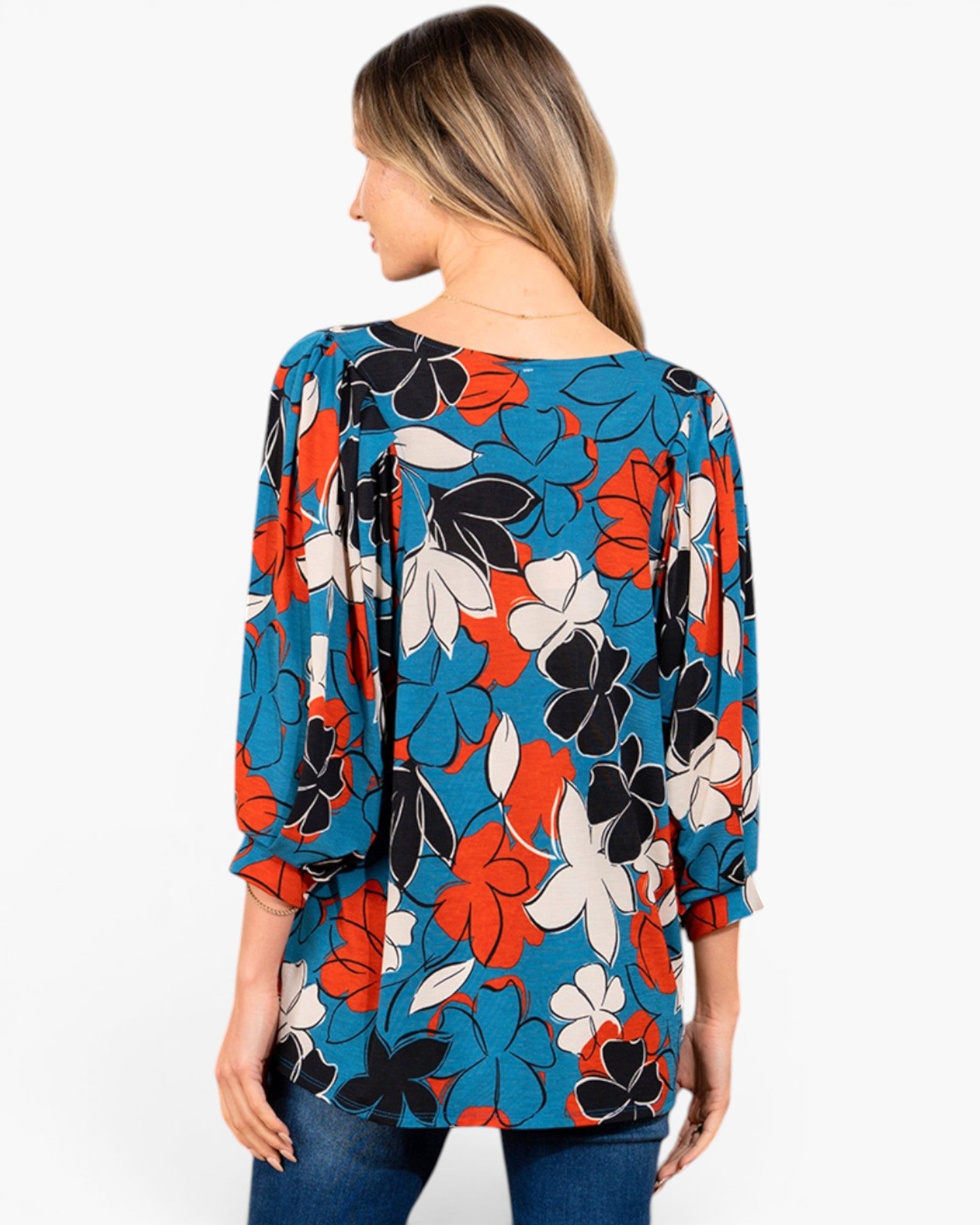 A woman shown from the back wearing a loose, three-quarter sleeve top with a bold floral print in blue, orange, black, and white, paired with blue jeans against a plain white background.