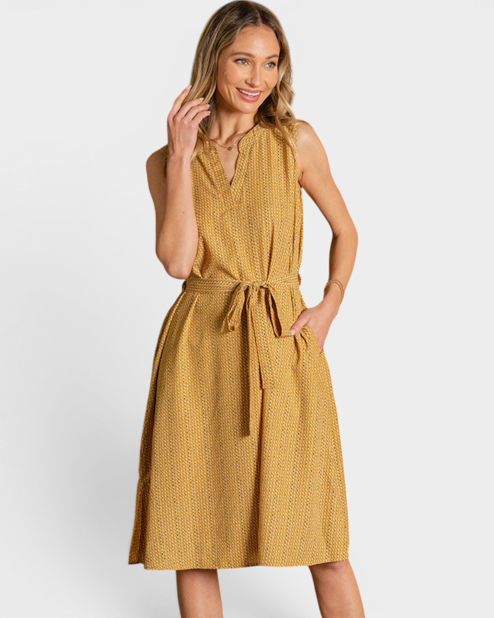 A woman modeling a sleeveless mustard yellow textured dress with a tie waist and V-neckline, photographed against a light gray studio background.