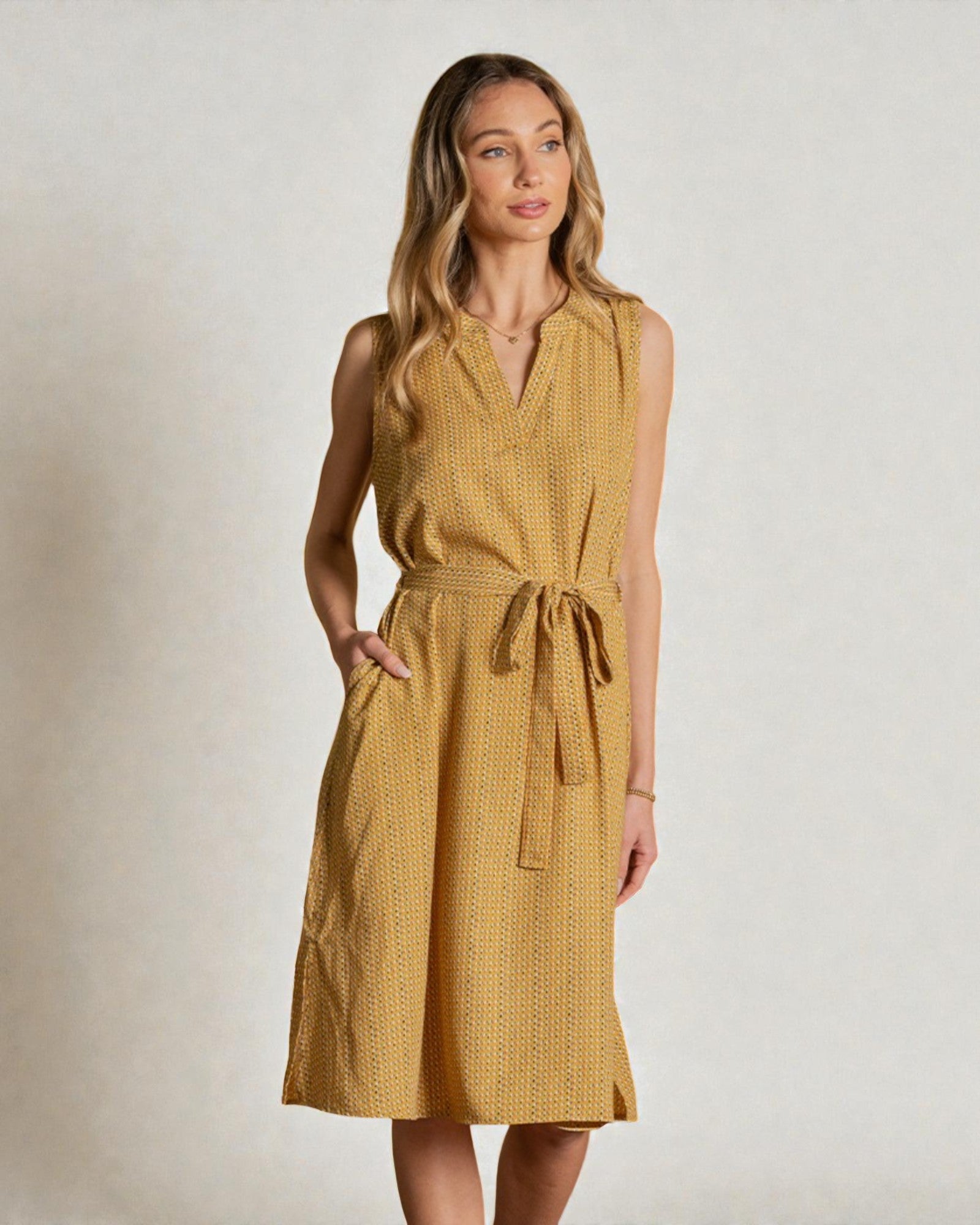 Woman wearing a mustard yellow dress with a belt against a plain background