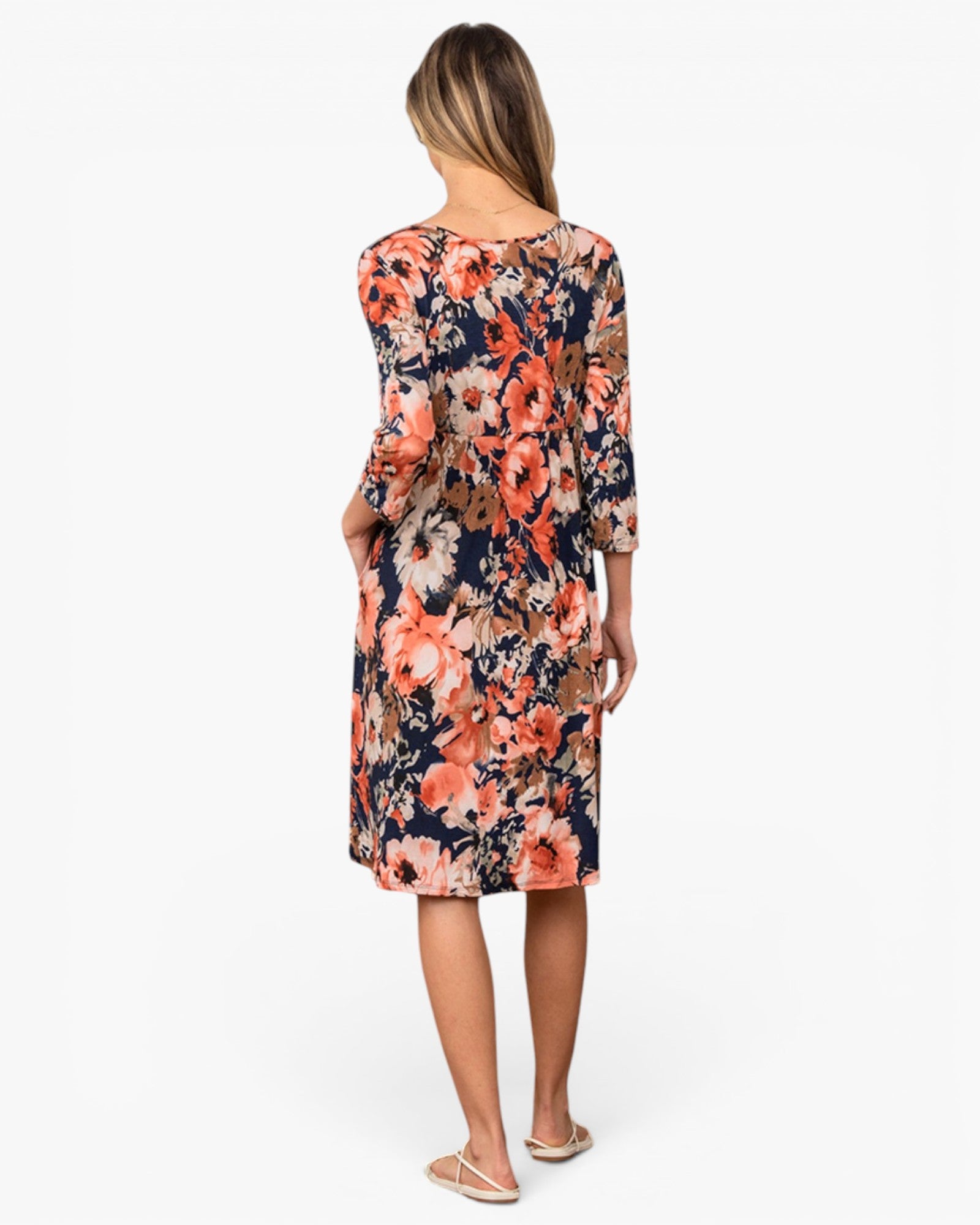 A woman viewed from behind wearing a knee-length floral dress with three-quarter sleeves on a plain white studio background.