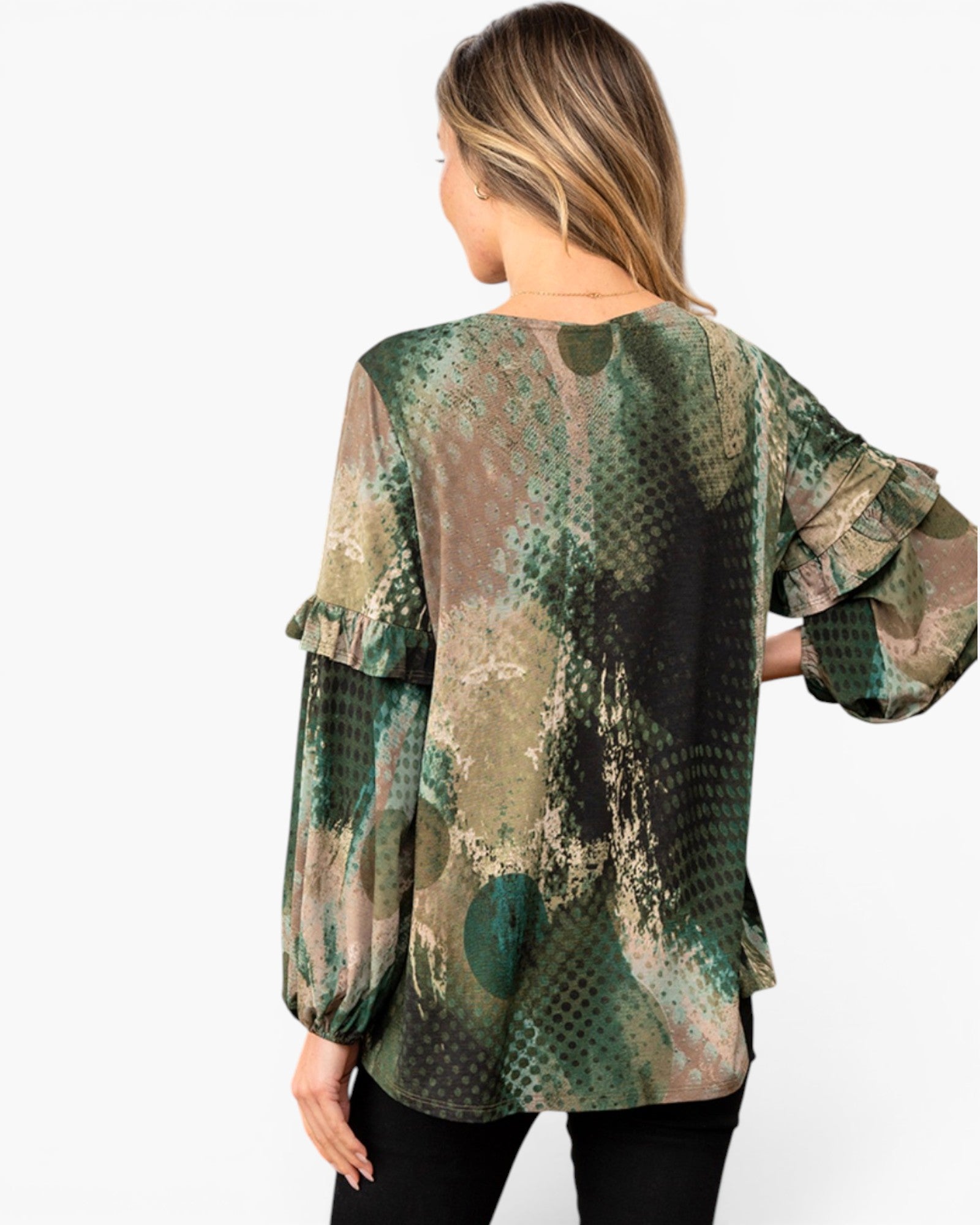A woman shown from the back wearing a long-sleeve blouse with a green, brown, and beige abstract pattern and ruffled cuffs, paired with black pants, against a plain white background.