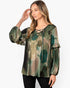 A woman modeling a long-sleeve blouse with a green, brown, and beige abstract pattern, featuring a lace-up neckline and ruffled sleeves, set against a plain white background.