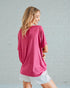 Woman wearing a pink oversized shirt and white shorts against a gray brick wall.
