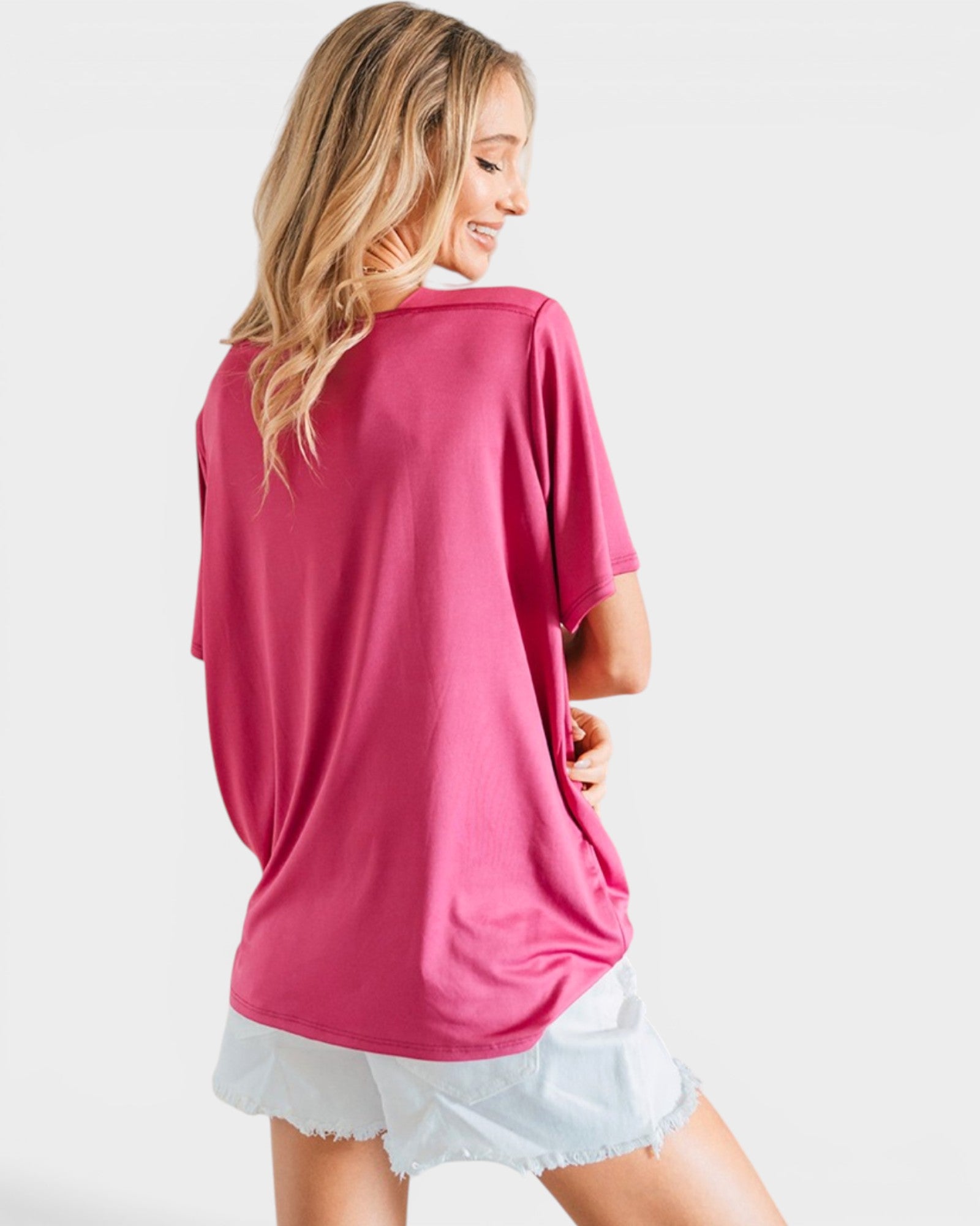 A woman shown from the back wearing a loose-fitting, short-sleeve pink t-shirt and light denim shorts against a plain light gray background.