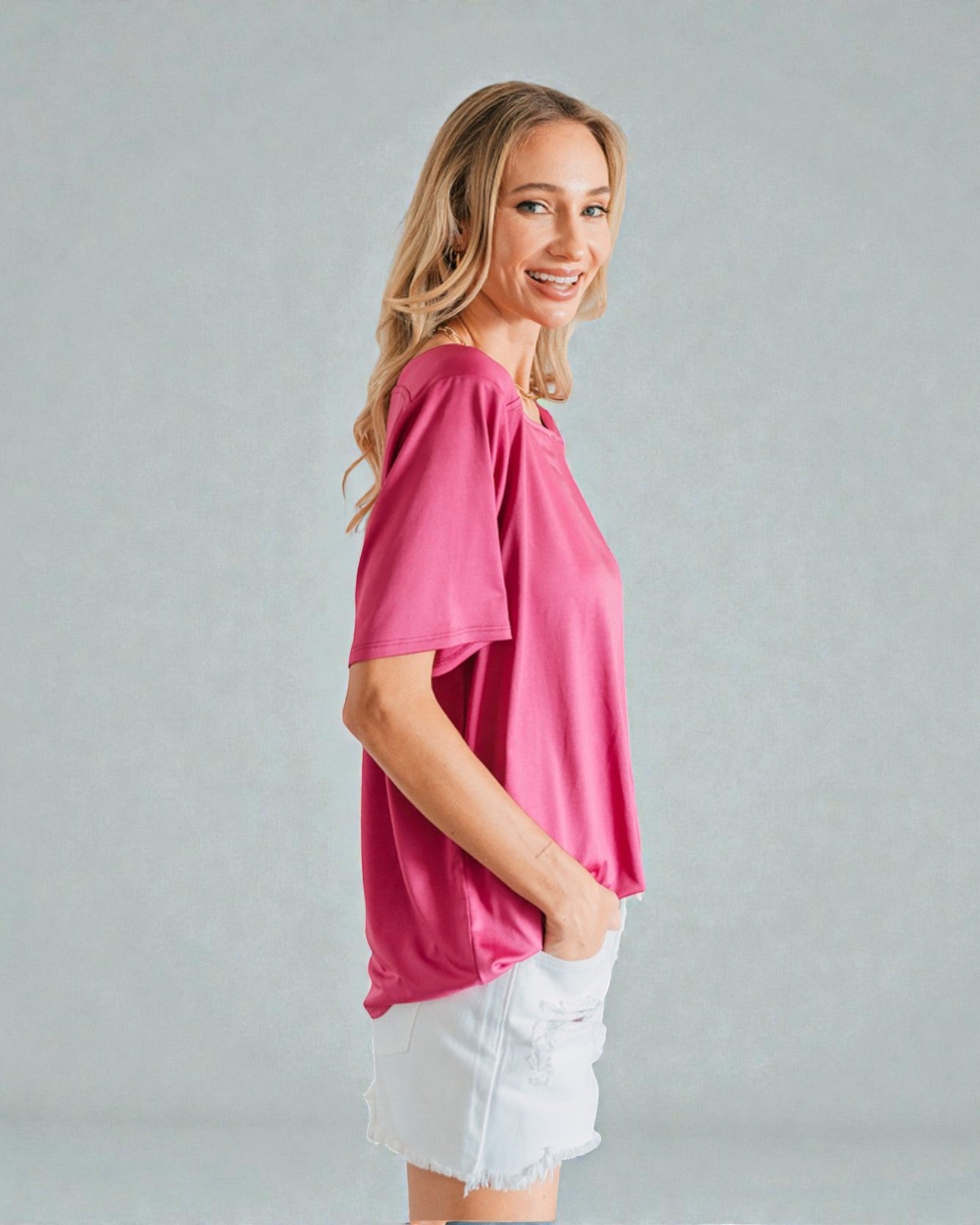 Woman wearing a pink top and white shorts against a gray background