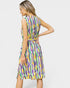A woman modeling a sleeveless knee-length dress with a colorful abstract wavy pattern in purple, yellow, green, and white, shown from a three-quarter back angle against a light gray studio background.