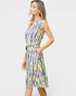 A woman modeling a sleeveless knee-length dress with a colorful abstract wavy stripe pattern in purple, green, yellow, and white, featuring a tie waist belt, set against a plain light gray background.