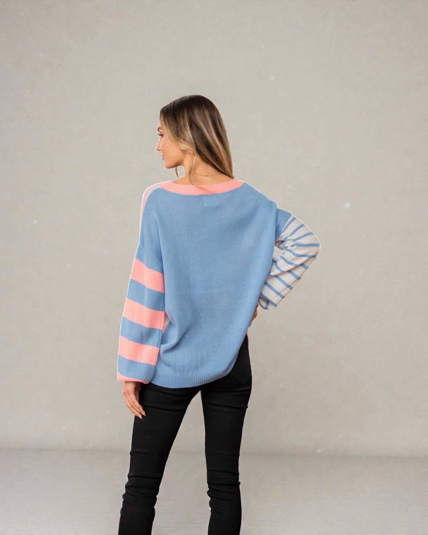 Woman wearing a blue sweater with pink and striped sleeves against a plain background