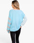 A woman shown from the back wearing a light blue knit sweater with striped sleeves, paired with black pants, against a plain white studio background.