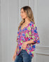 Woman wearing a colorful floral blouse against a gray wall
