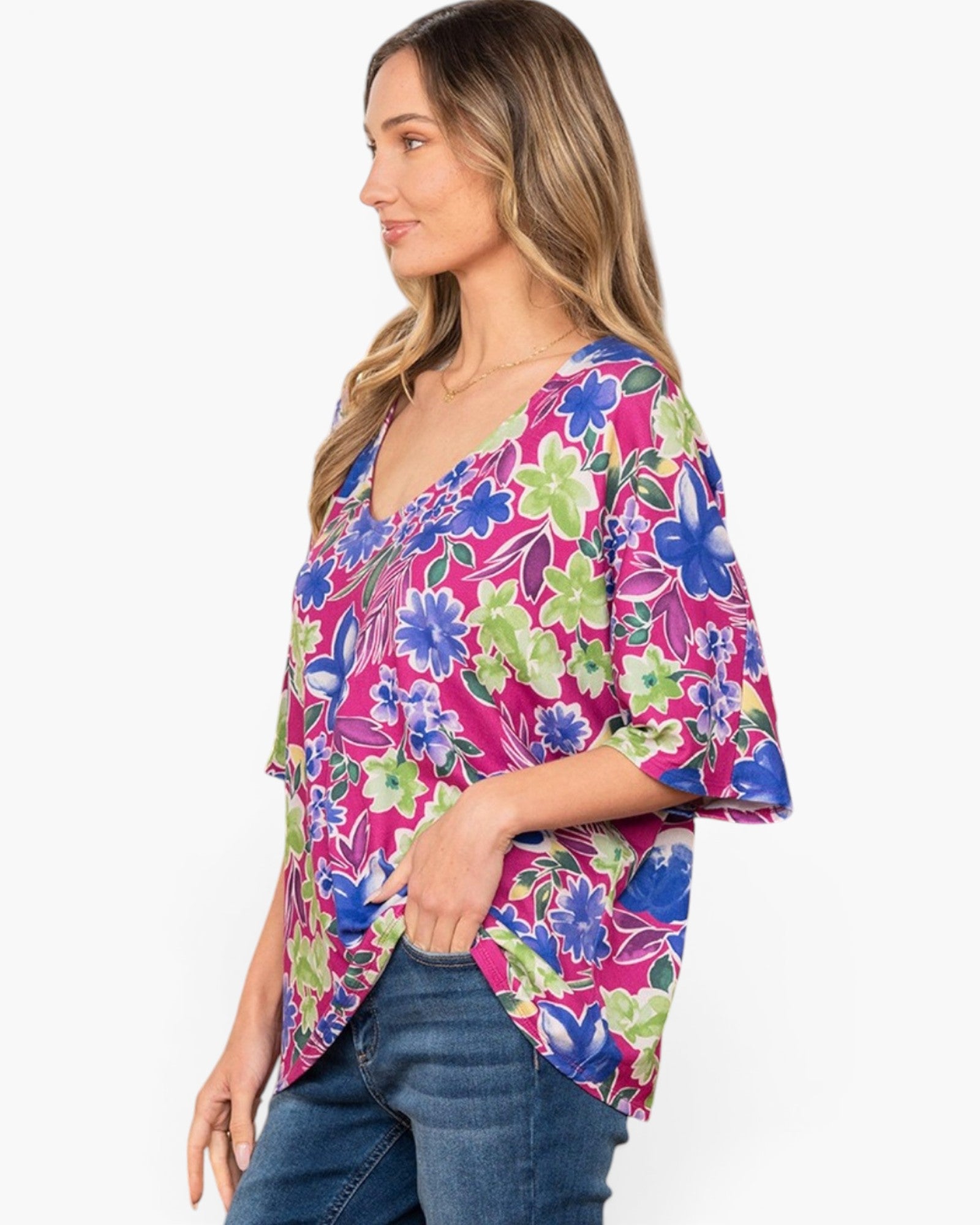 A woman wearing a vibrant floral print top with blue, green, and pink flowers, paired with blue jeans, shown from a side profile against a plain white background.