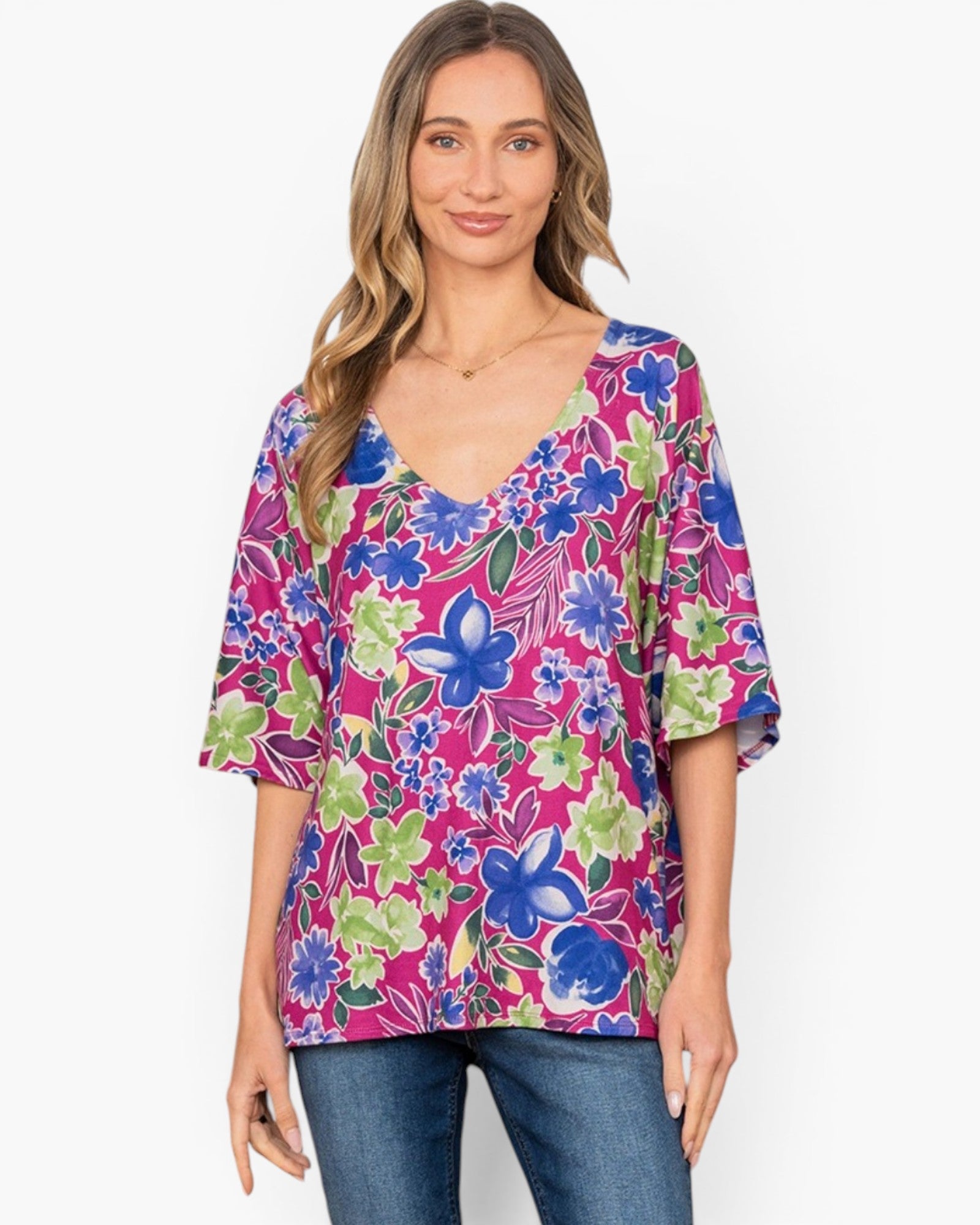 A woman wearing a vibrant floral print top with blue, green, and pink flowers, paired with blue jeans, against a plain white background.