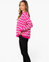A woman modeling a bright pink and white chevron pattern knit sweater, paired with black pants, against a plain white studio background.