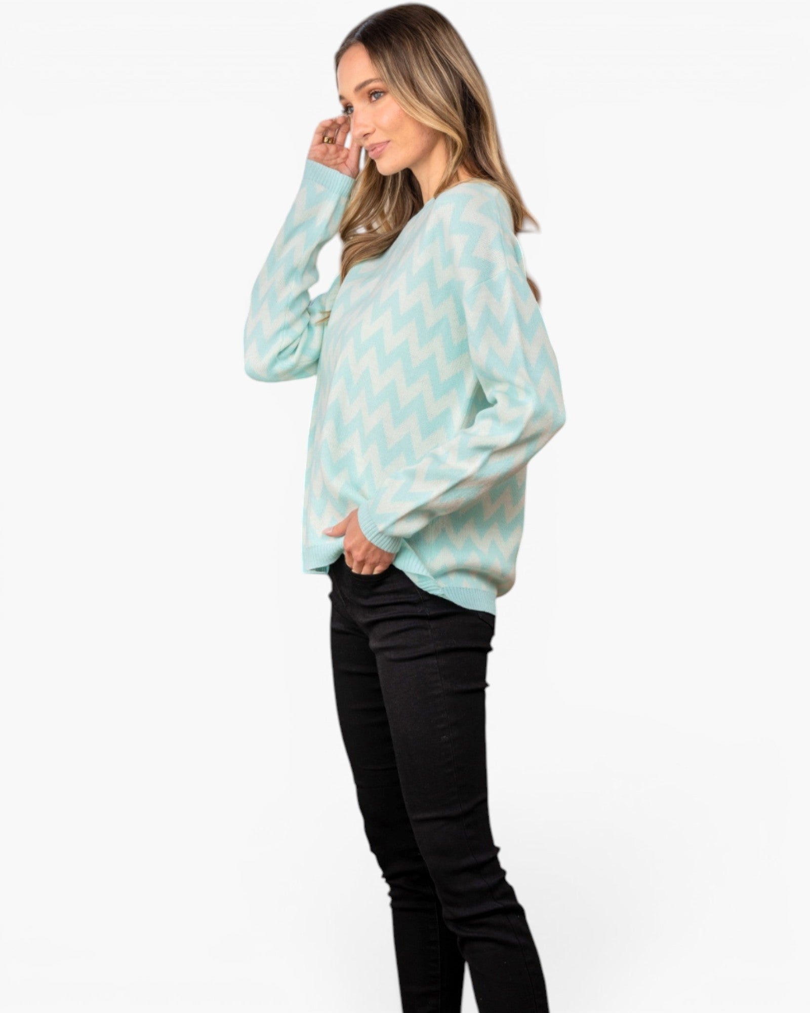 A woman modeling a light mint green and white chevron knit sweater with black pants, shown from a side profile against a plain white studio background.