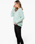 A woman modeling a light mint green and white chevron knit sweater with black pants, shown from a side profile against a plain white studio background.
