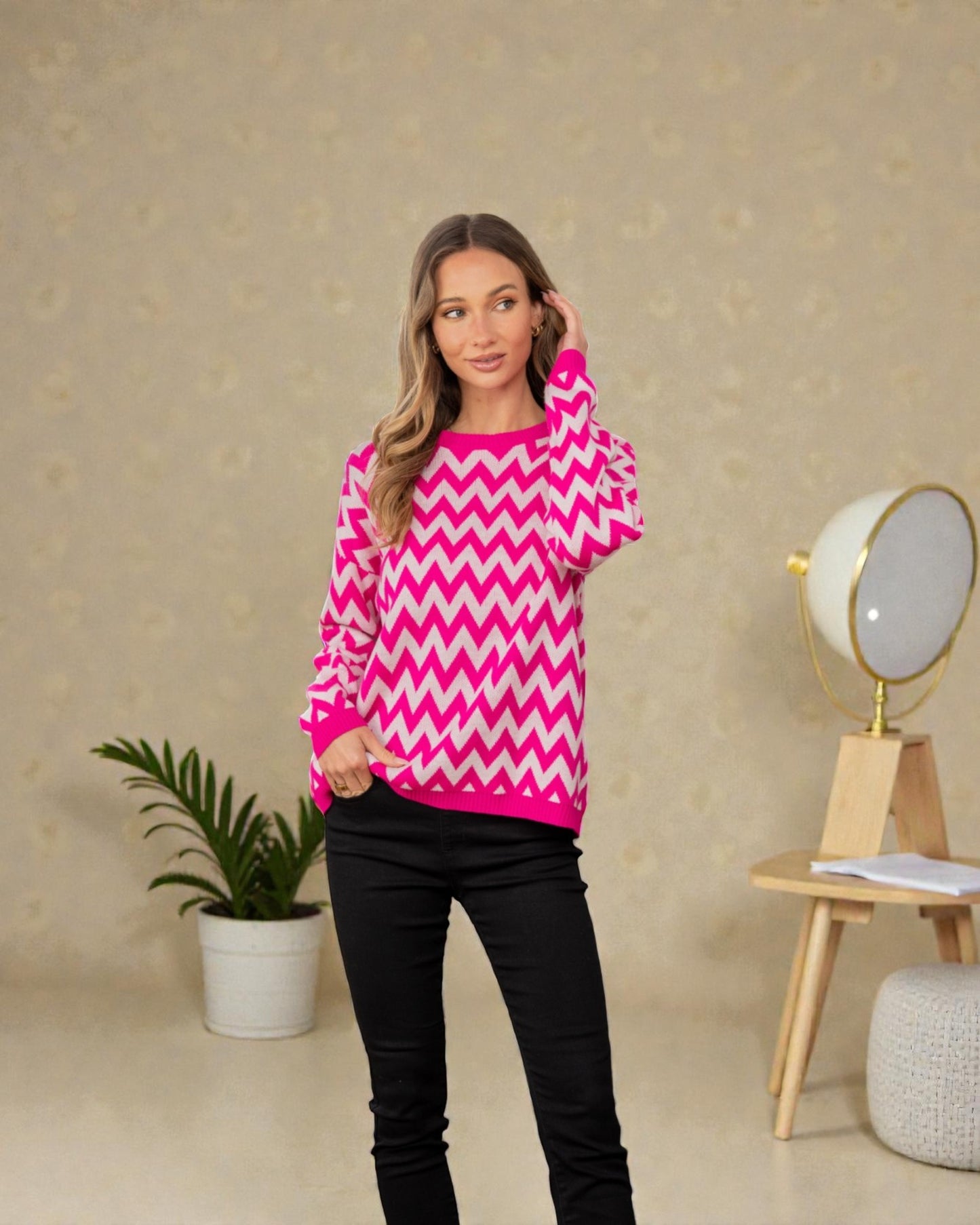 Woman wearing a pink and white zigzag sweater in a room with a plant and lamp.
