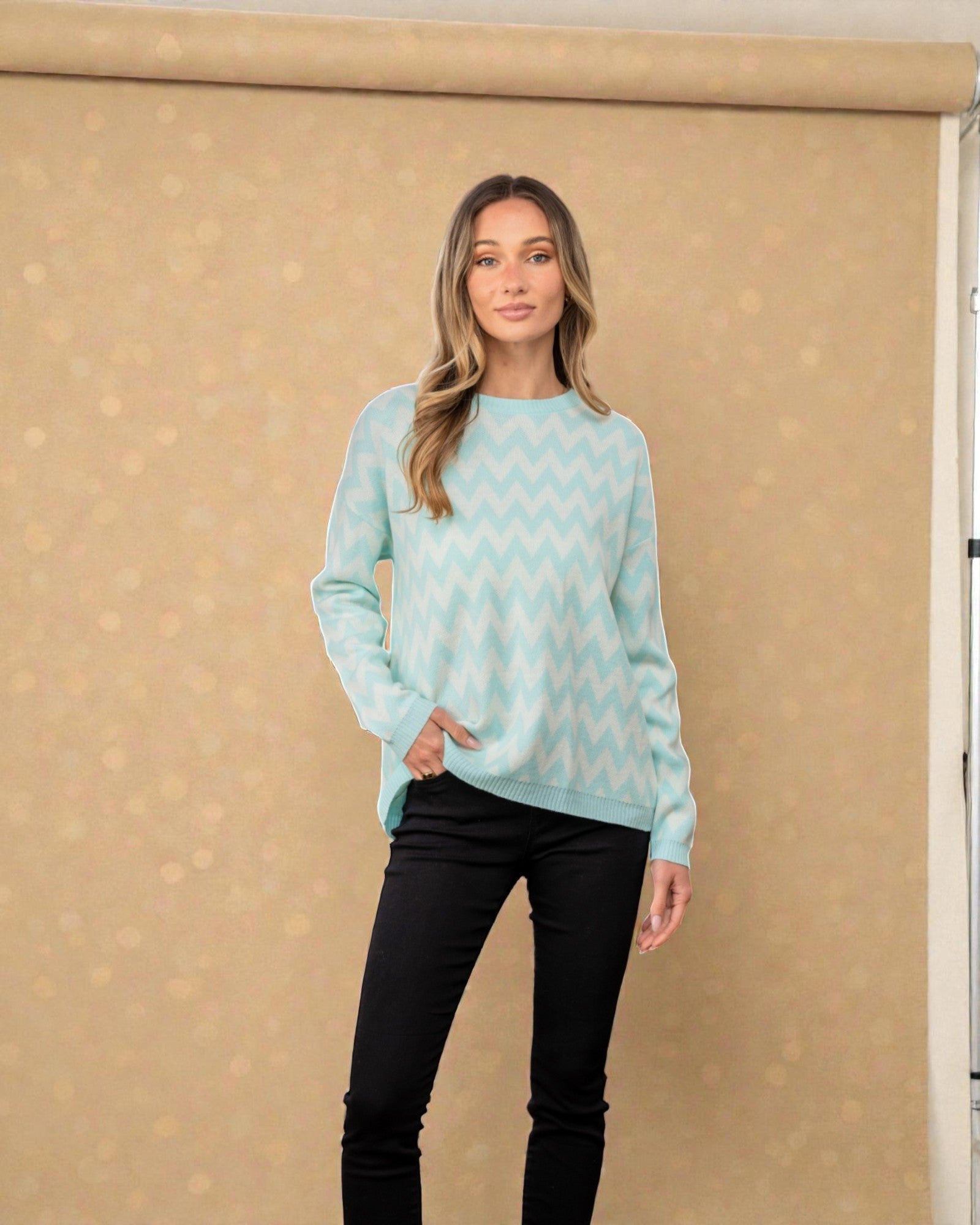 Woman wearing a light blue patterned sweater and black pants against a beige background