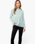 A woman modeling a mint green and white chevron-patterned knit sweater with black pants, standing against a plain white studio background.