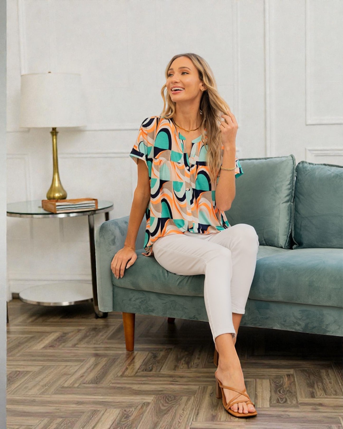 Woman sitting on a blue couch in a living room, wearing a colorful patterned top and white pants.
