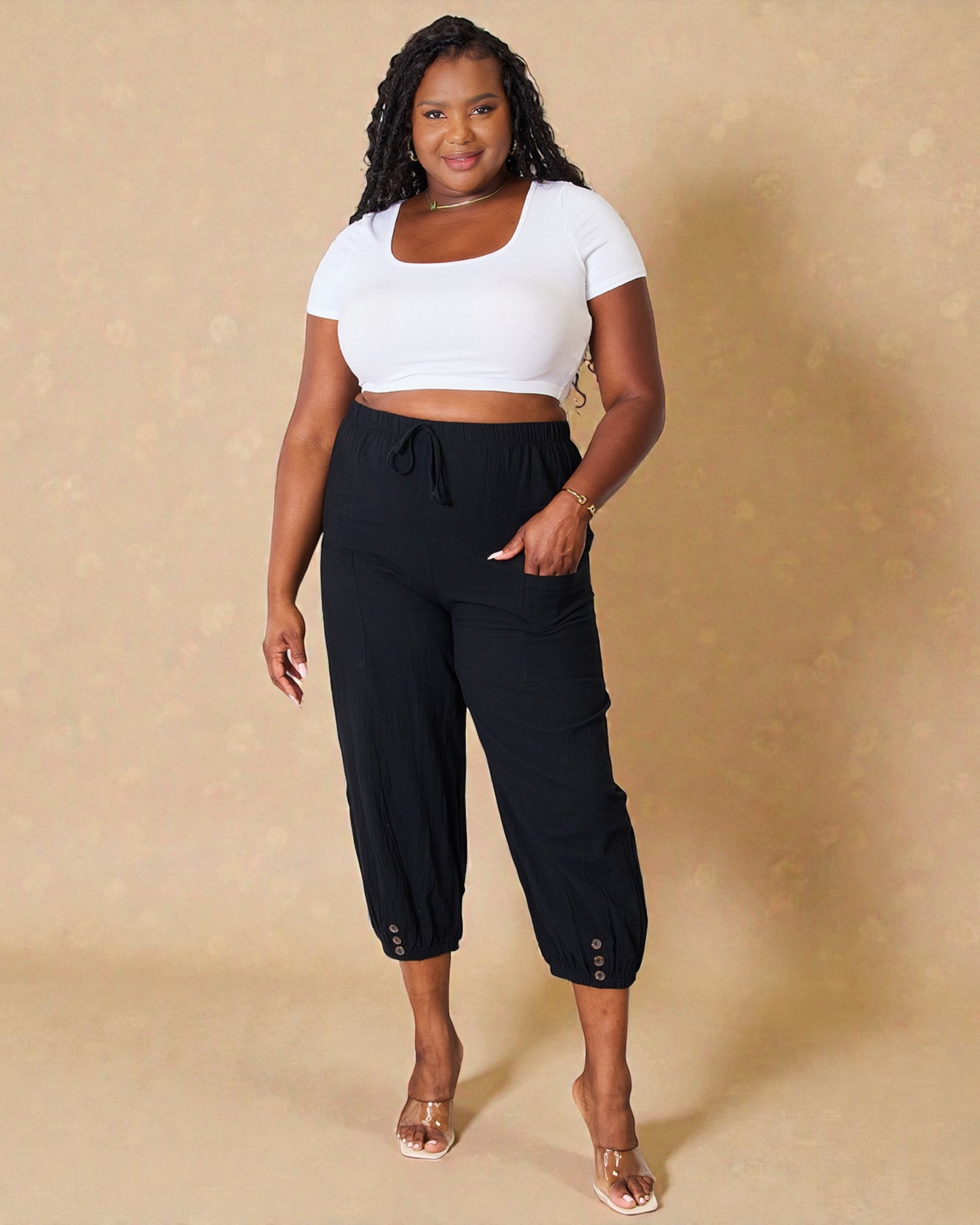 Woman wearing a white crop top and black pants against a beige background