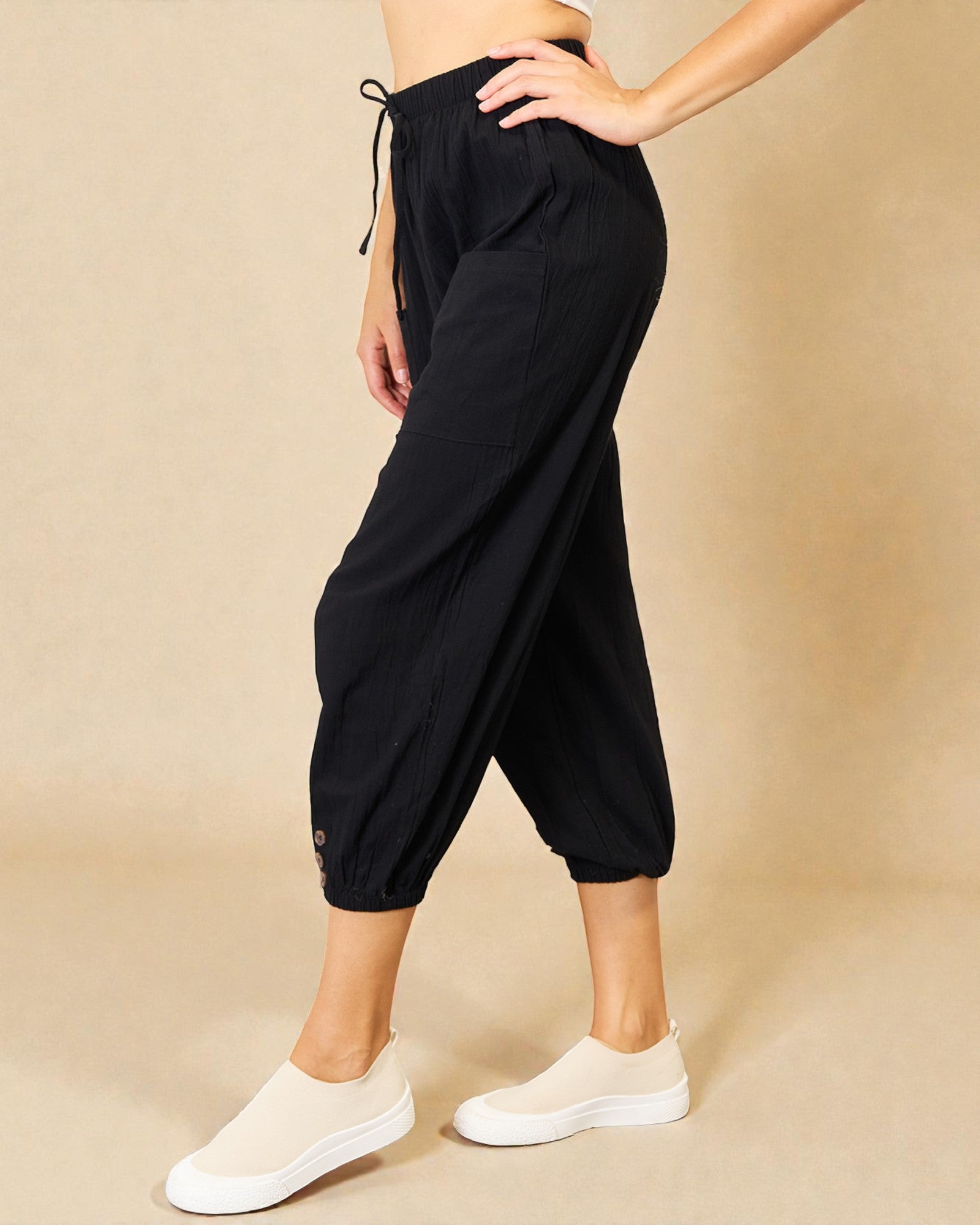 Person wearing black capri pants and white sneakers on a beige background