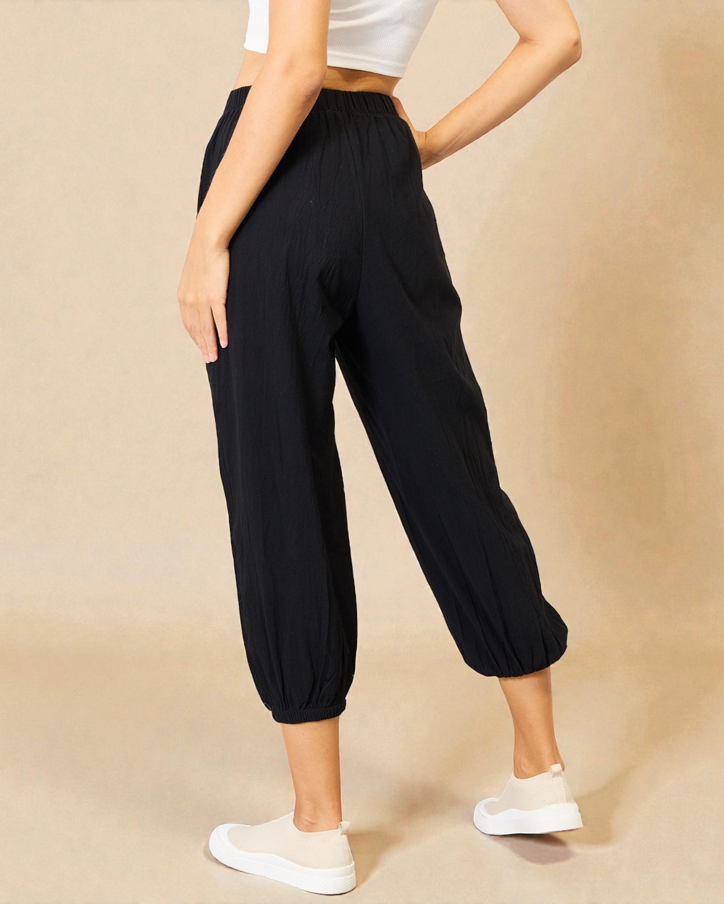 Person wearing black pants and white sneakers on a beige background