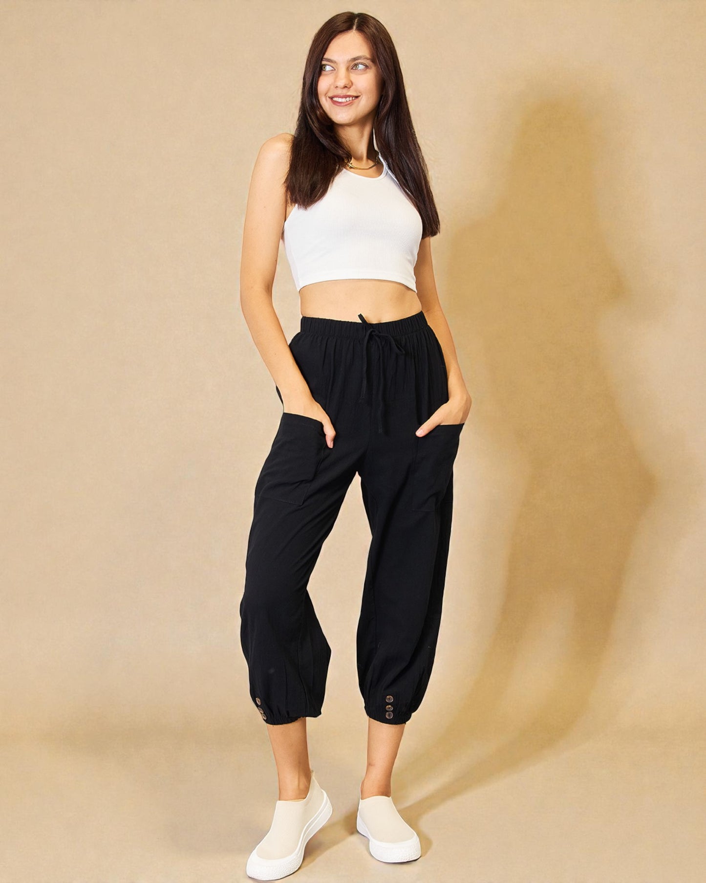 Woman wearing a white crop top and black high-waisted pants on a beige background