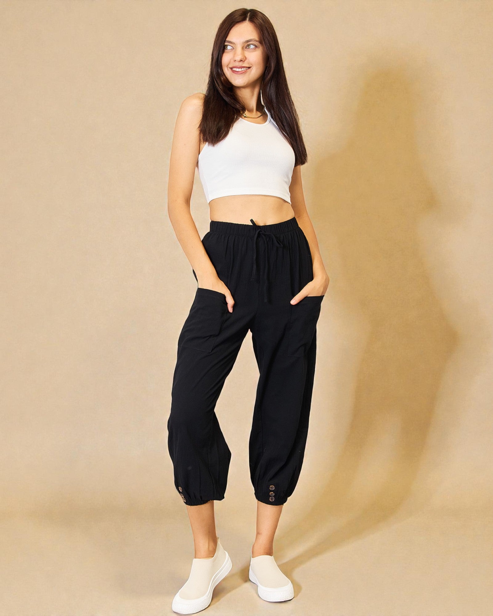 Woman wearing a white crop top and black high-waisted pants on a beige background