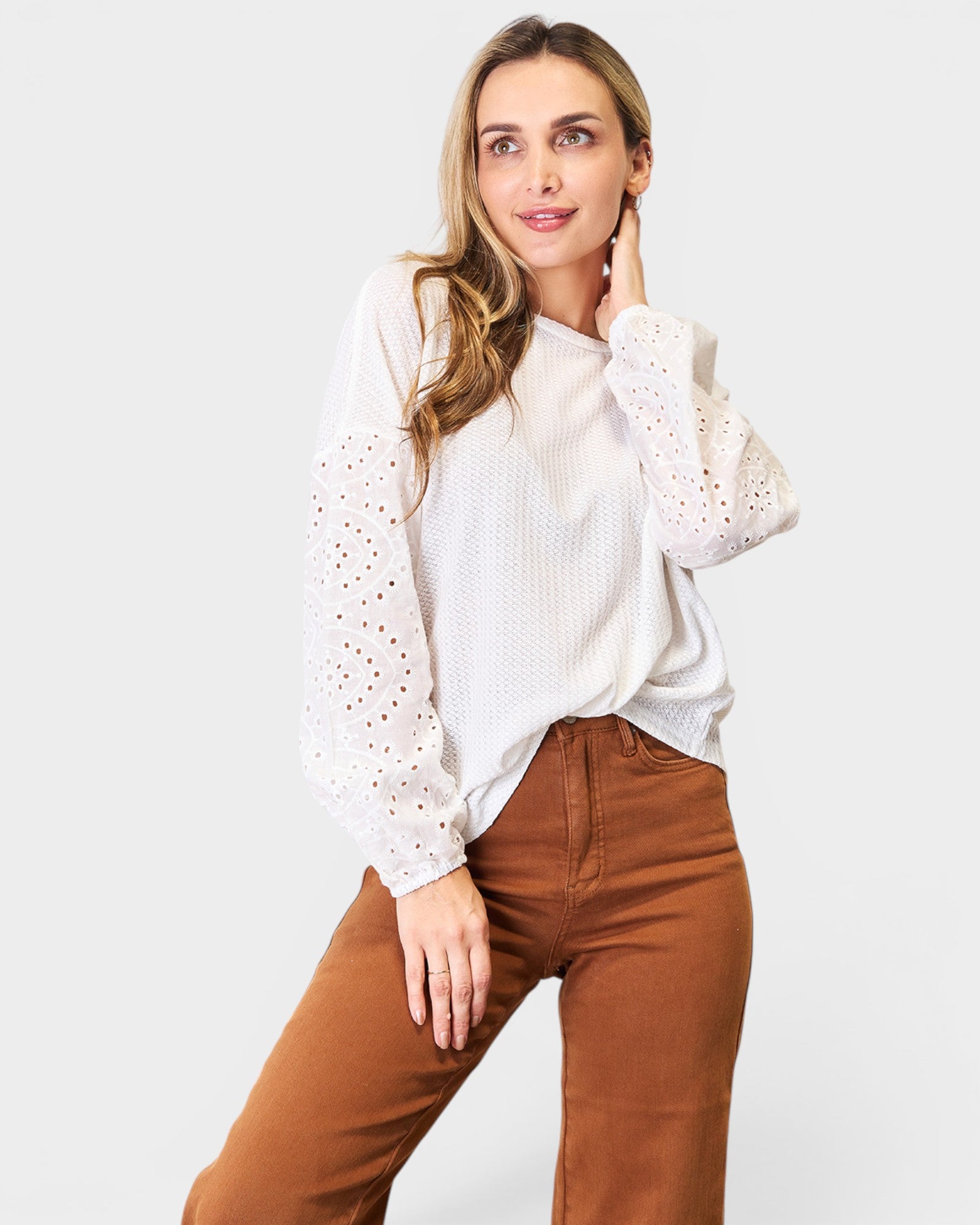 Woman wearing a white blouse with lace details and brown pants on a white background