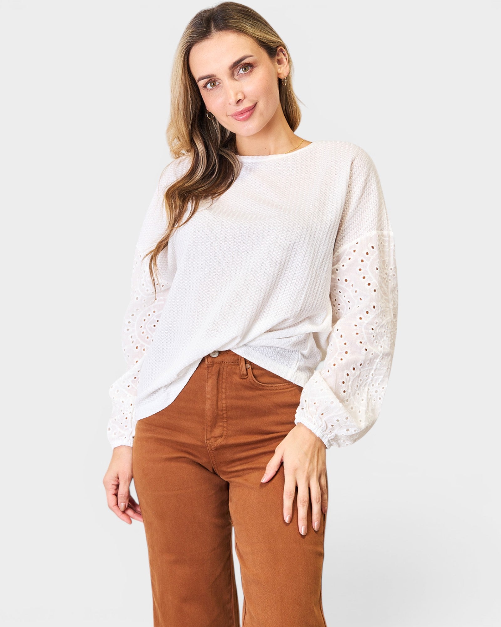 Woman wearing a white blouse with lace details and brown pants on a white background