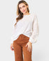 Woman wearing a white blouse with lace details and brown pants on a white background