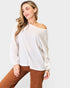 Woman wearing a white off-shoulder sweater with brown pants on a light gray background