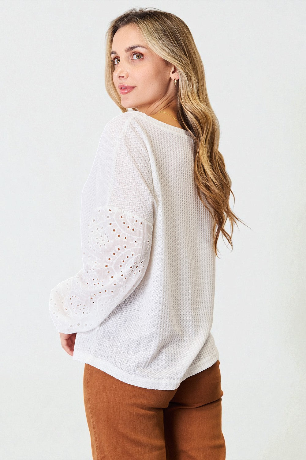 Woman wearing a white sweater with lace sleeves against a white background