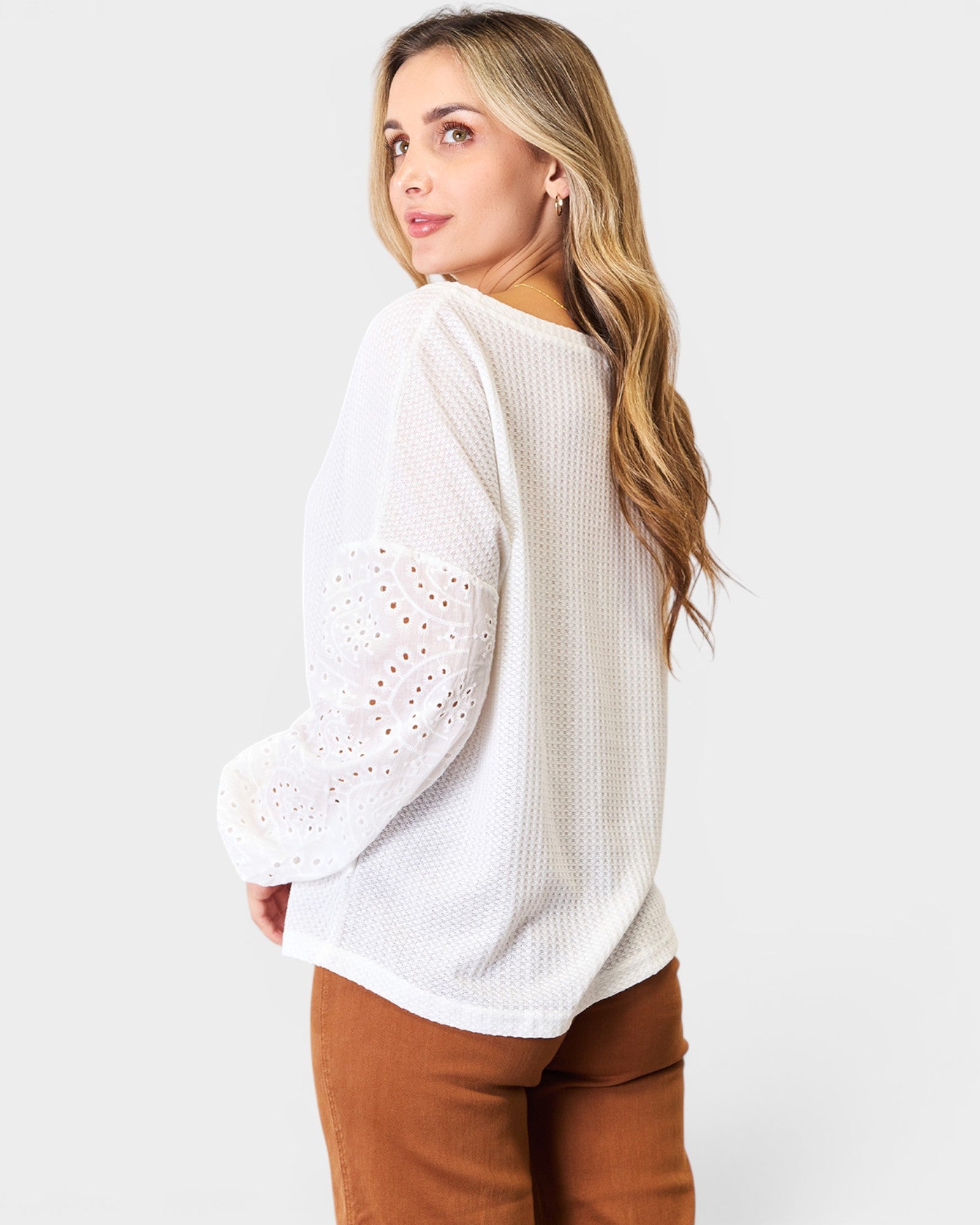 Woman wearing a white sweater with eyelet details on a plain background