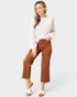 Woman wearing a white blouse and brown pants on a plain background