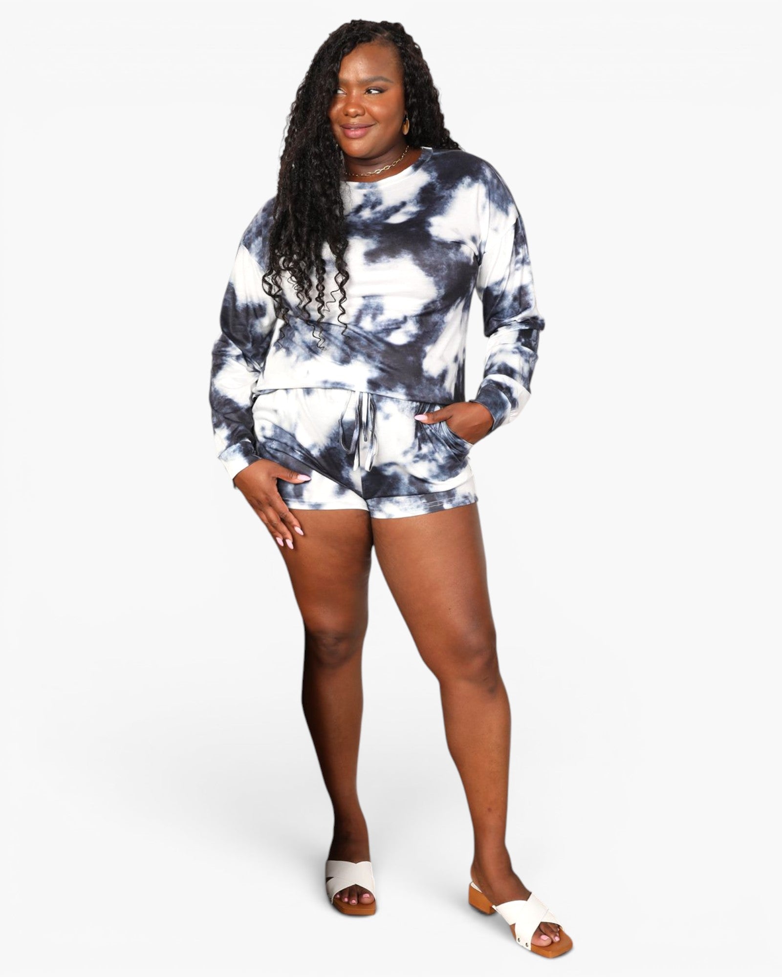A woman modeling a matching long-sleeve sweatshirt and shorts set with a navy and white tie-dye pattern, paired with white slide sandals, against a plain light gray background.