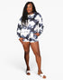 A woman modeling a matching long-sleeve sweatshirt and shorts set with a navy and white tie-dye pattern, paired with white slide sandals, against a plain light gray background.