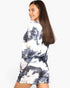 A woman modeling a matching long-sleeve top and shorts set with a navy blue and white tie-dye pattern, shown from a three-quarters back view against a plain white background.