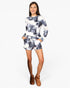 A woman modeling a matching long-sleeve top and shorts lounge set in a navy and white tie-dye pattern, paired with brown ankle boots, against a light gray studio background.