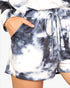 Close-up of a person wearing tie-dye shorts with a blue-gray and white cloud pattern, featuring side pockets and a matching drawstring waist.