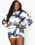 A woman modeling a matching long-sleeve top and shorts set in a black and white tie-dye pattern, standing against a light gray studio background.