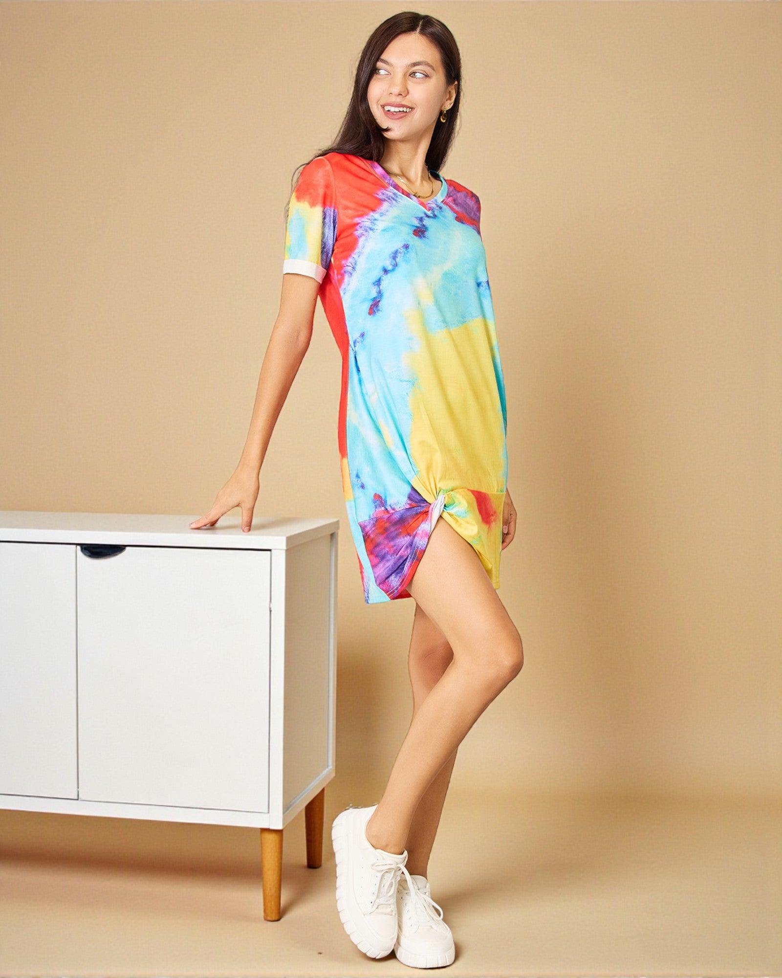 Woman wearing a colorful tie-dye dress standing next to a white cabinet on a beige background