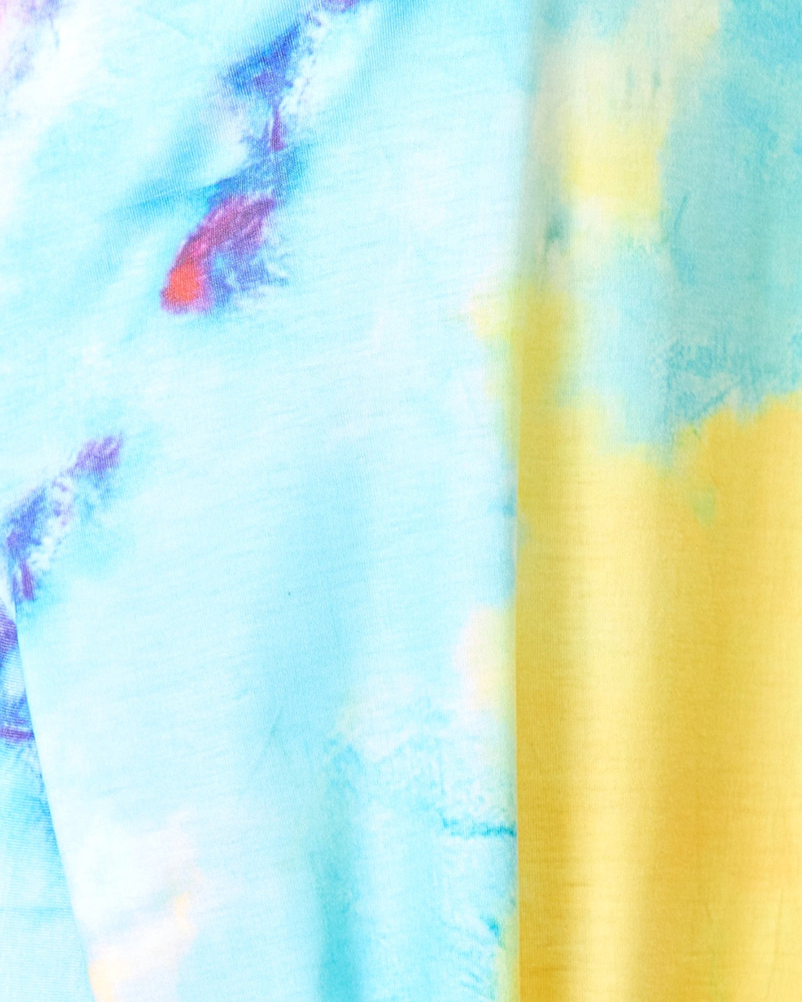 A close-up of a tie-dye fabric with a light blue base, a prominent yellow vertical stripe, and small purple and red watercolor-like accents.