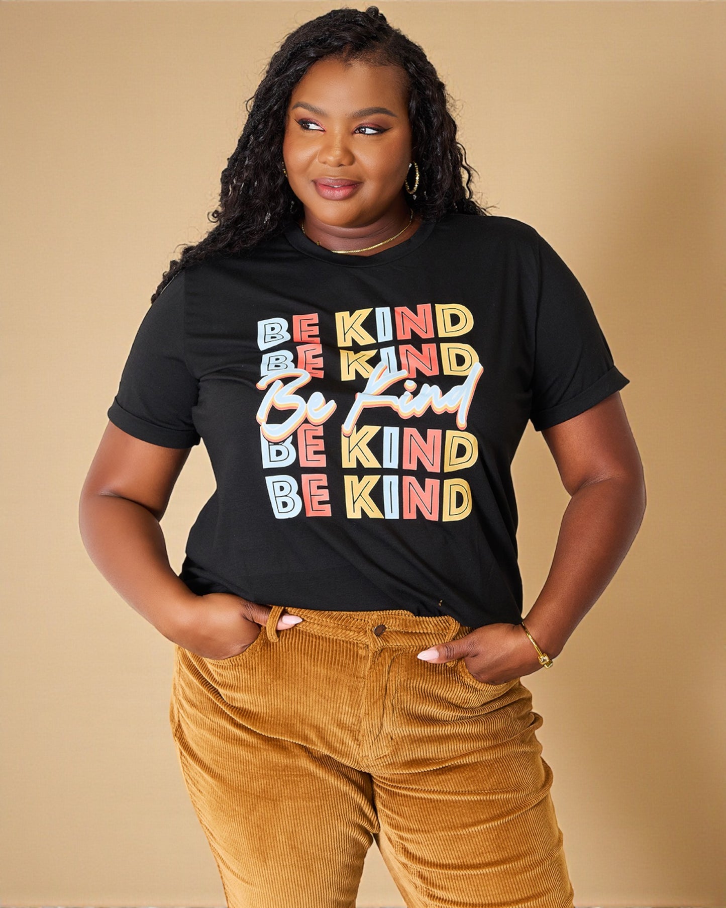 Person wearing a black t-shirt with 'Be Kind' text in multiple colors on a beige background