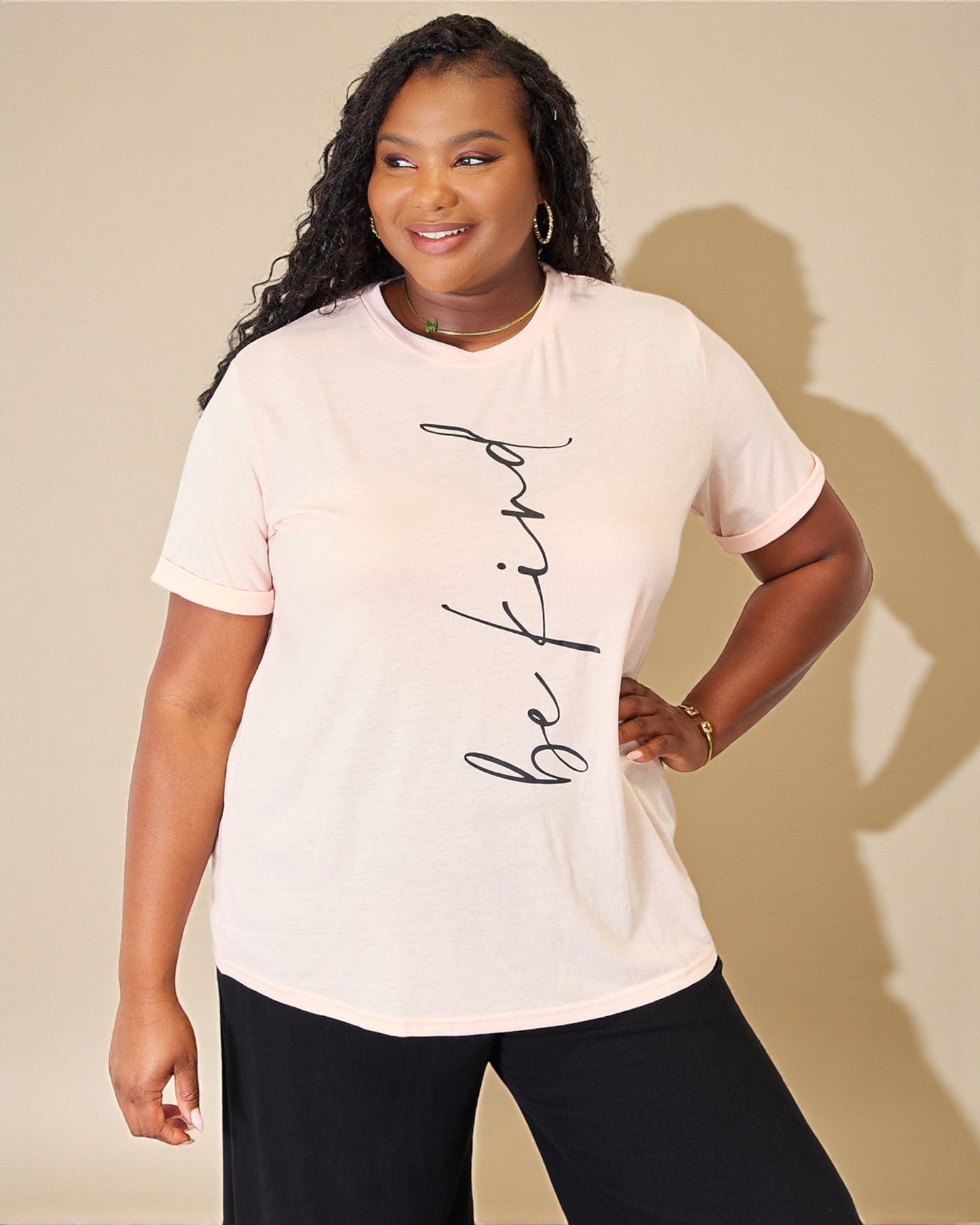 Woman wearing a white t-shirt with 'be kind' text against a beige background